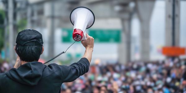 Mann mit Megaphone vor Menschenmenge